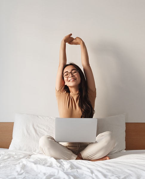 Rapariga relaxada com computador portátil sobre a cama num espaço de descanso.