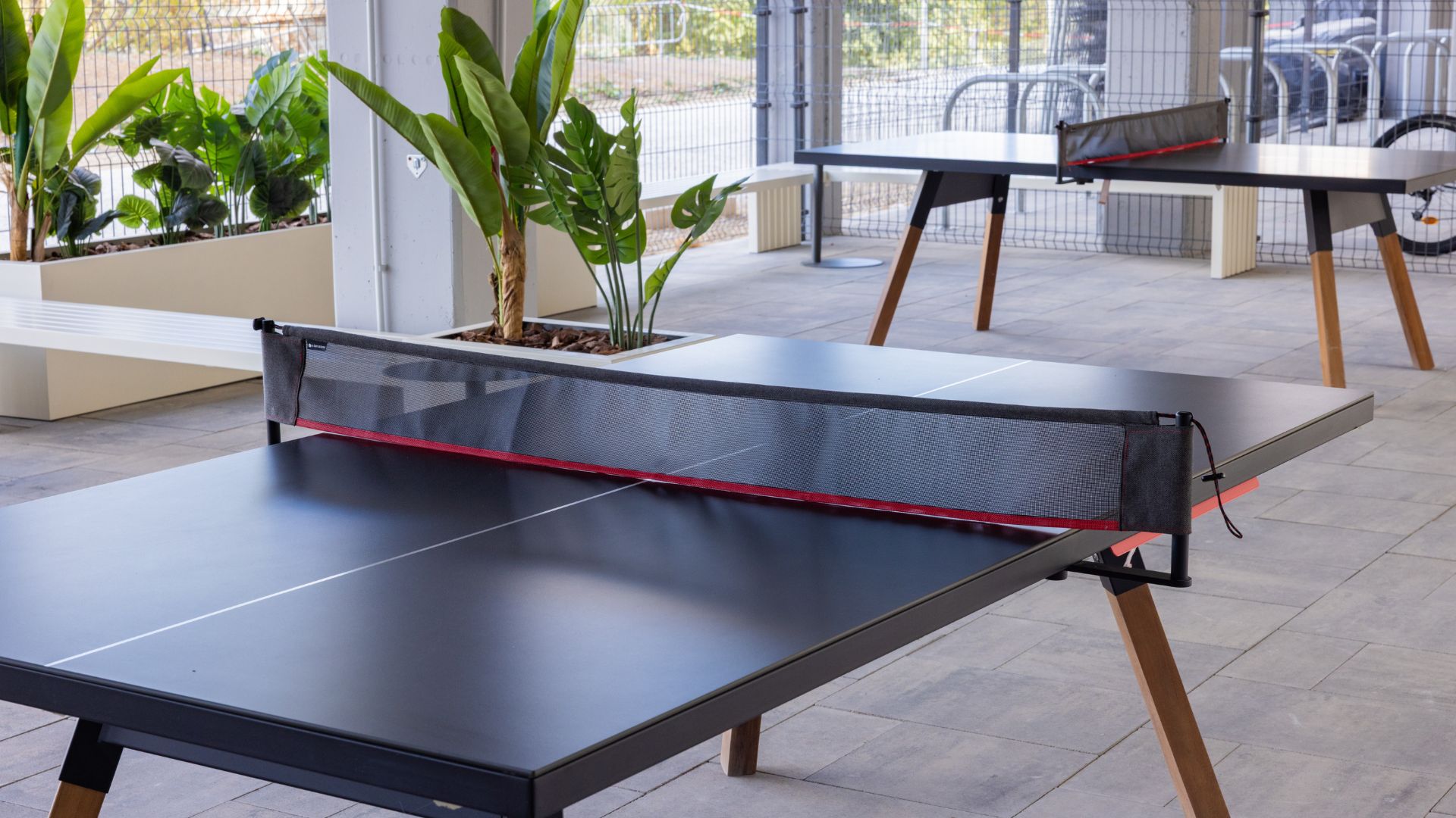 Zona exterior de juegos en la residencia universitaria de Cantoblanco, con mesas de ping pong y área ajardinada.