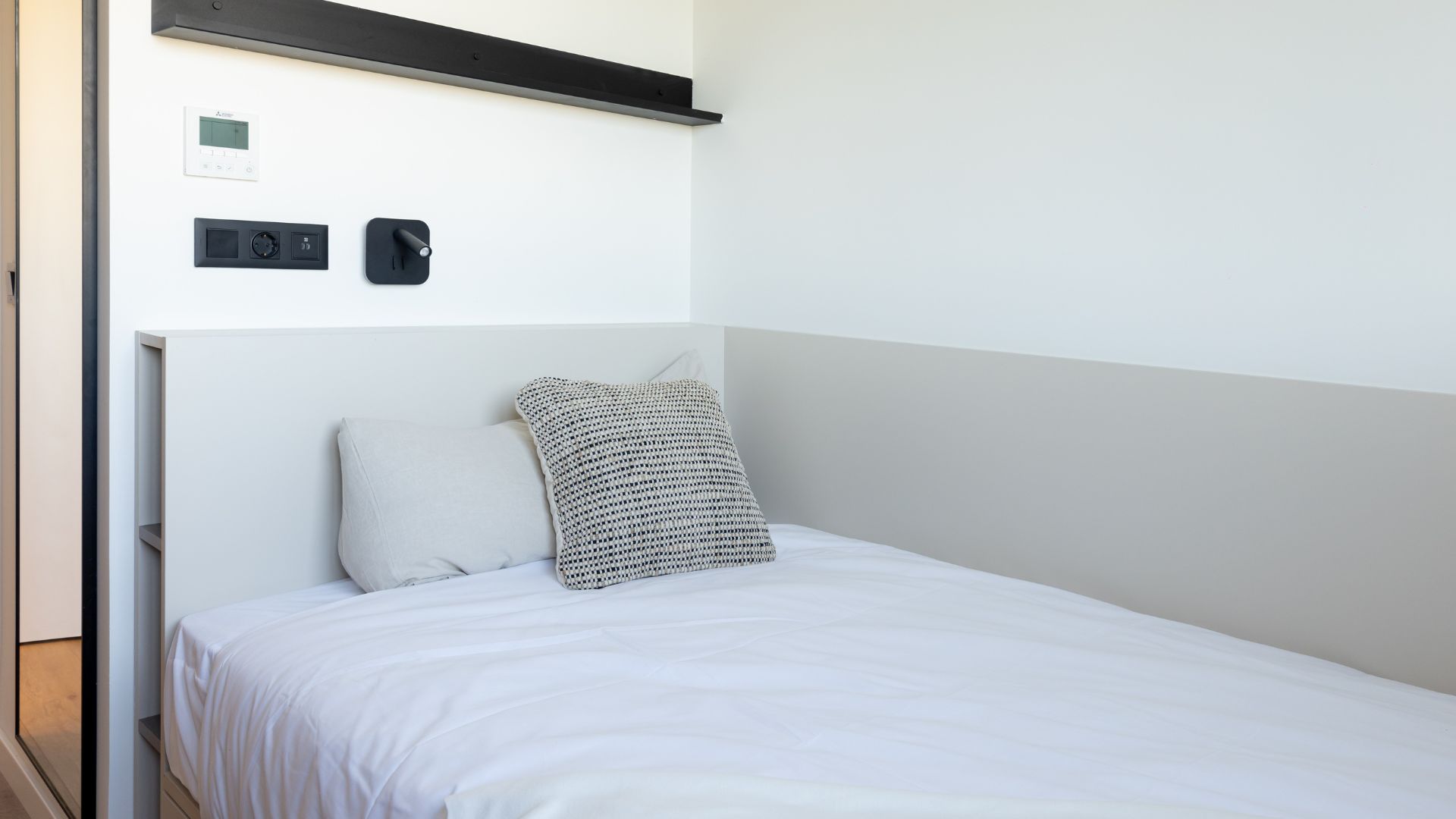 Cama individual del estudio junto a ventana, con luz natural y ambiente minimalista.