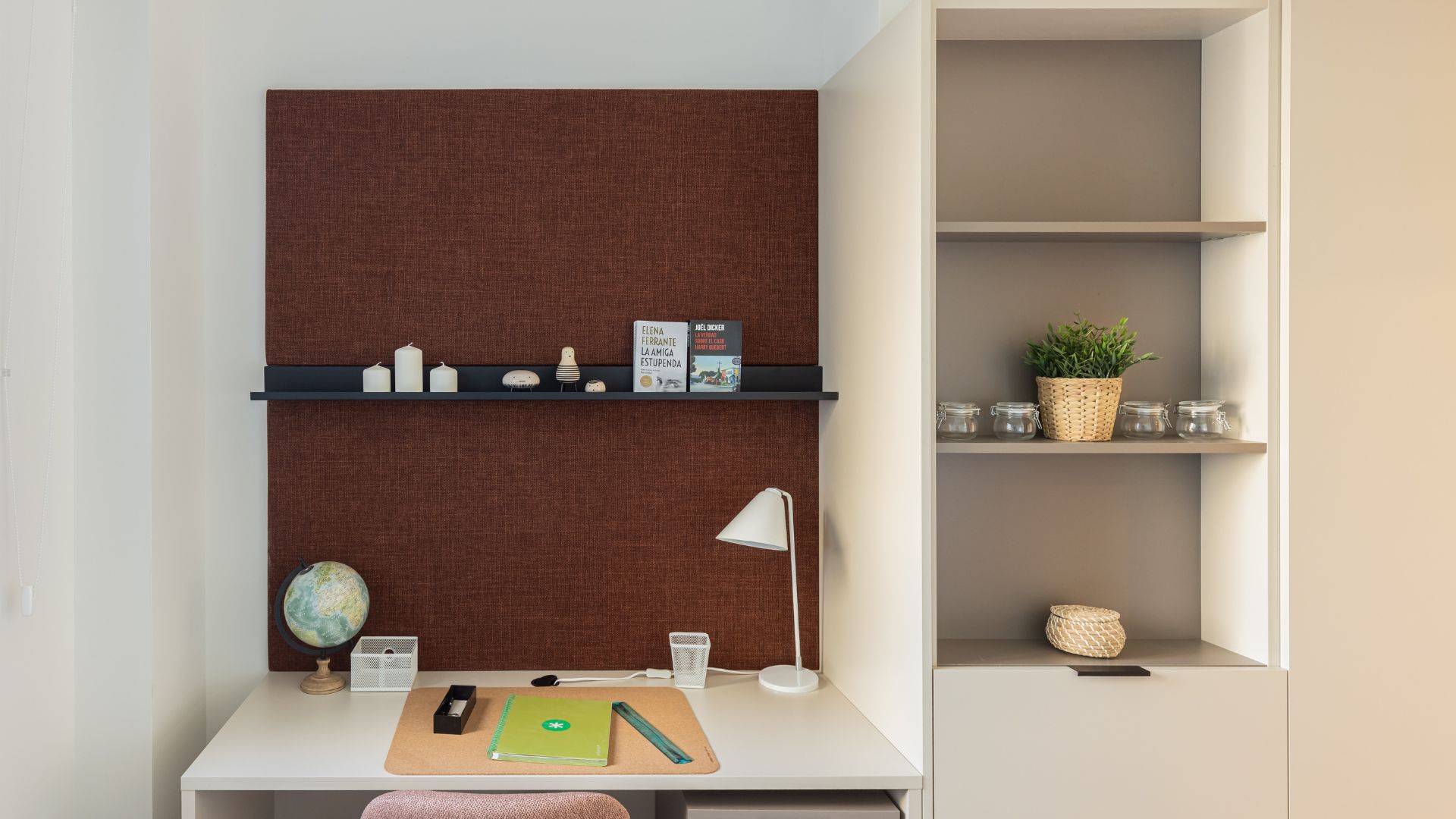 Escritorio de estudio moderno con iluminación integrada, silla tapizada, material de trabajo y decoración en tonos cálidos.