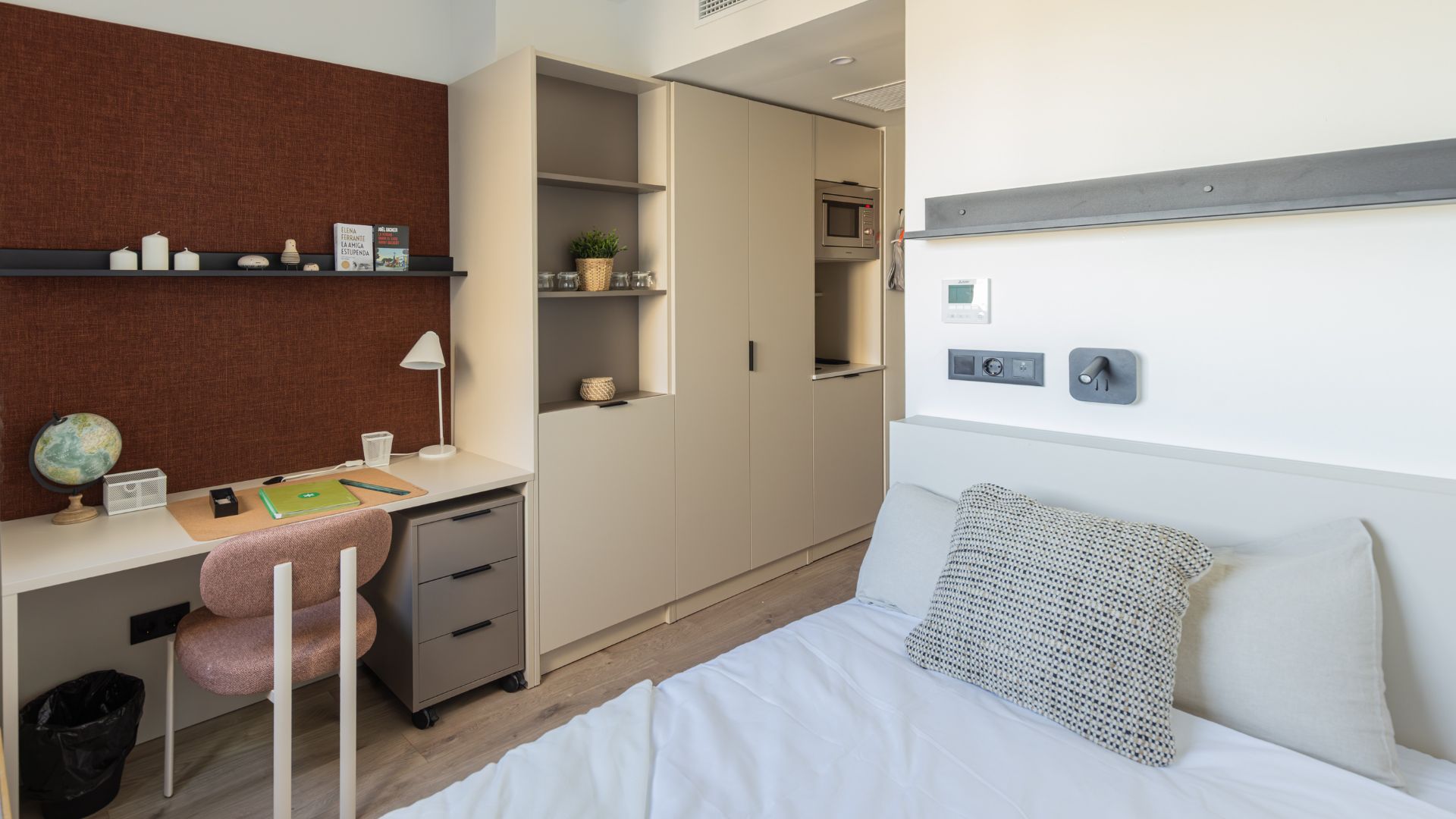 Vista general del estudio con cama, escritorio, armarios empotrados y cocina integrada de diseño moderno.