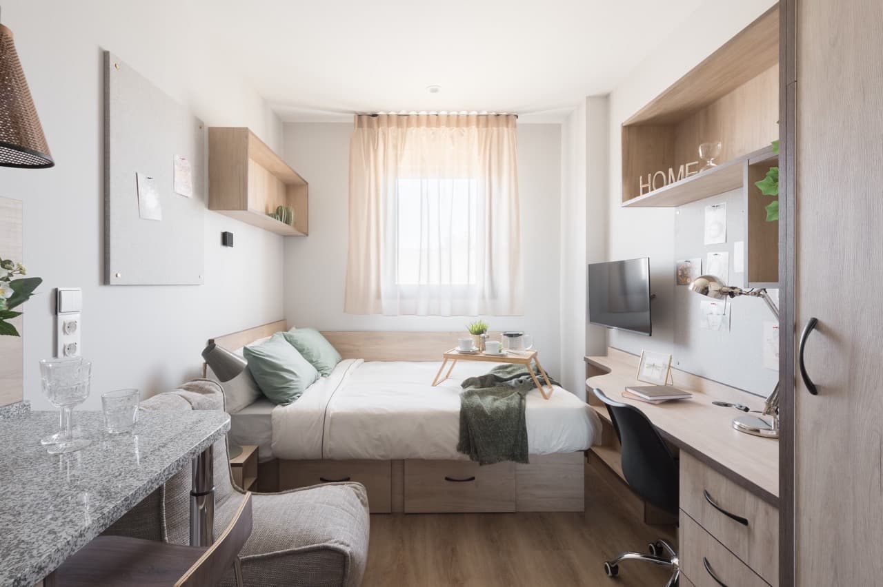 Cama preparada con sábanas, almohada y edredón en una habitación de estudiante