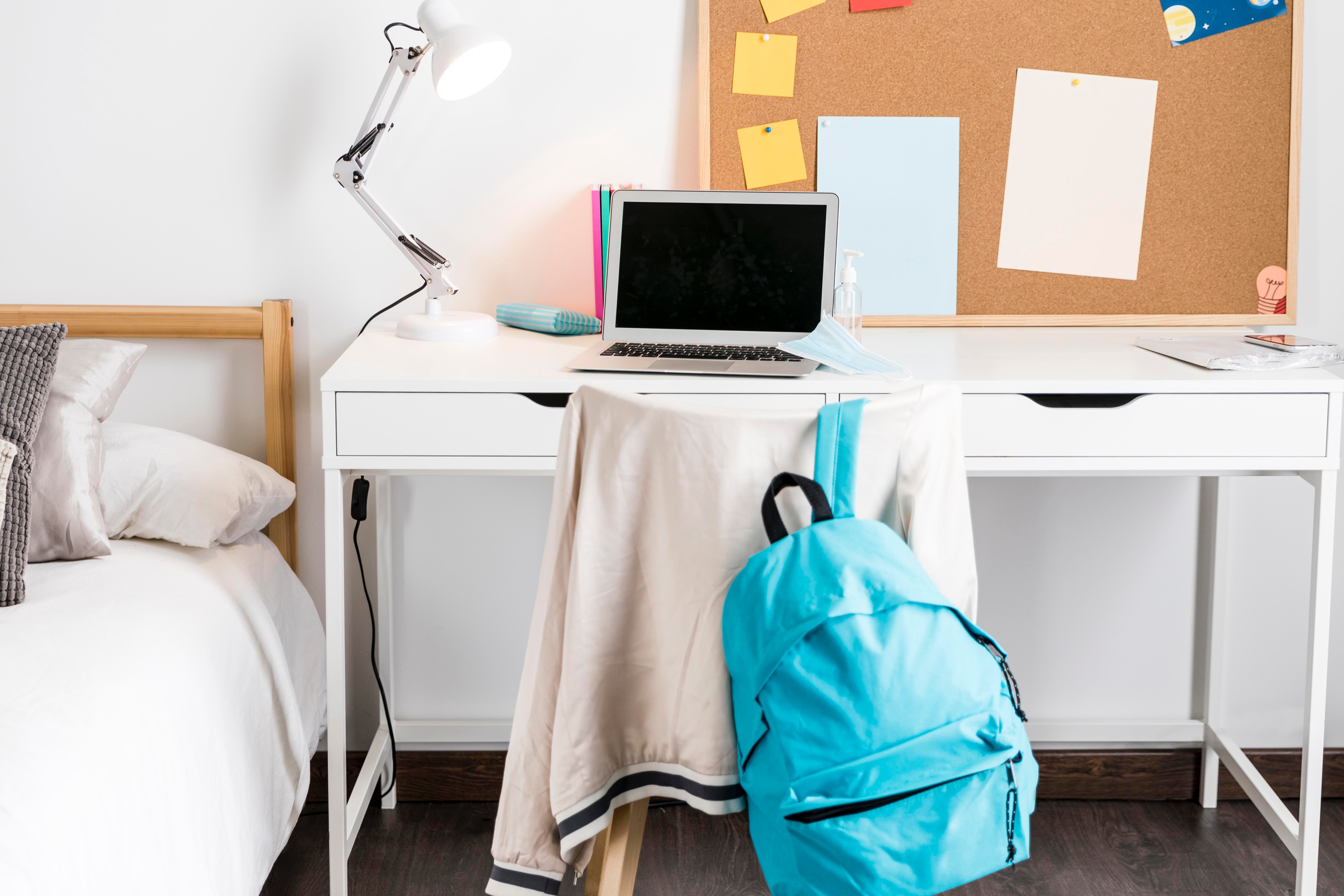 Escritorio con portátil, cuadernos y material escolar en habitación universitaria