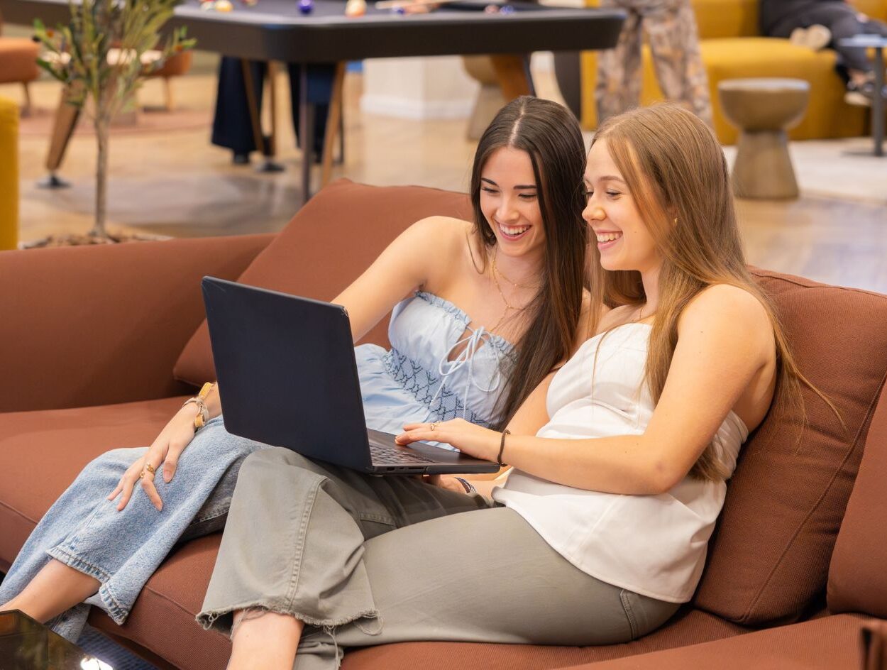 Estudiante universitaria trabajando con su ordenador portátil en una residencia de estudiantes, en un entorno moderno y luminoso.